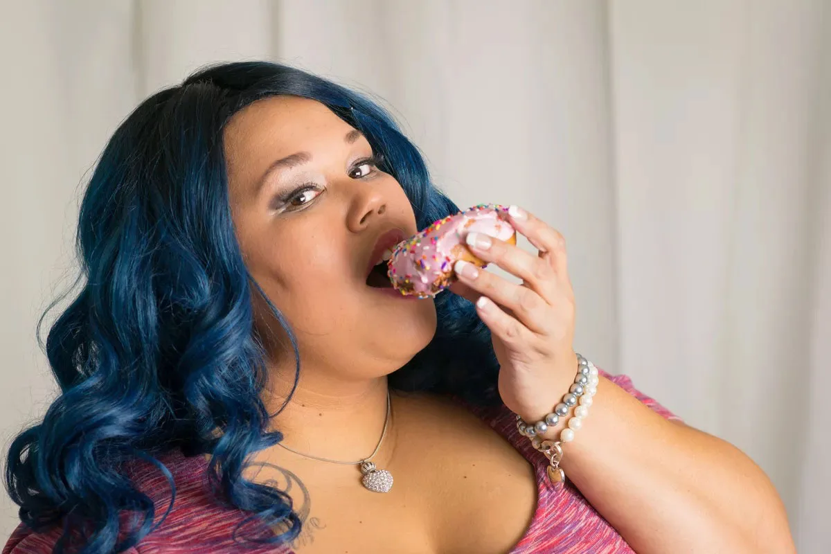 Woman in long curls eating pose with a donut in left hand