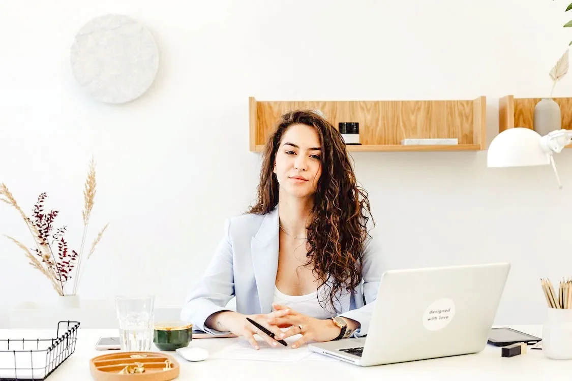 woman sitting in front of laptop on her desk with open hair in sky blue coat and white round neck t shirt
