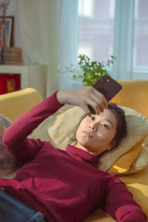 woman in dark maroon full neck full hands t shirt lying on a orange sofa holding phone in right hand - First Impressions Online