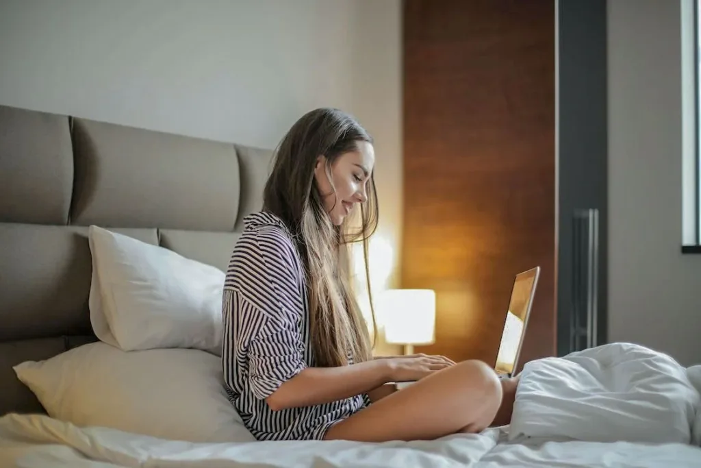 woman with long hair with striped black and white shirt sitting on bed with laptop - Online Dating for Busy Singles