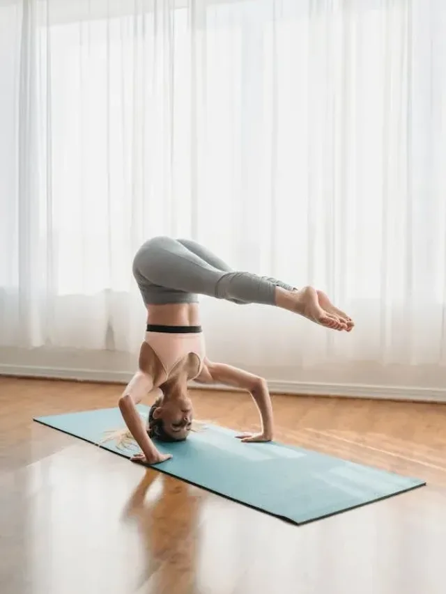 woman in pink sports bra and grey yoga pants doing headstand with legs folding in 90 degrees on a yoga mat