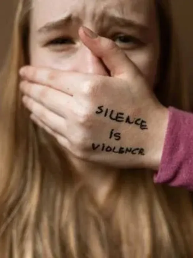 blonde long open hair and dark pink girl with worried eyebrows covered mouth silence is violence is written on her left hand