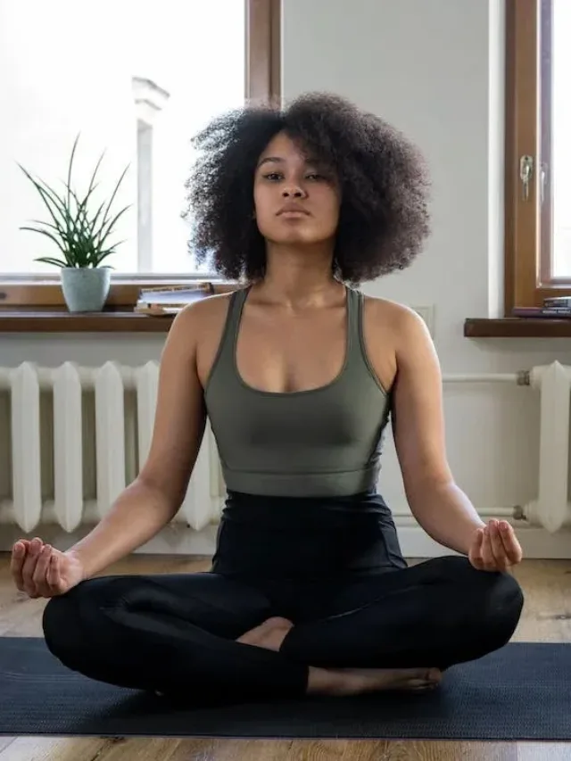 curly hair woman sitting in greyish t bag and black yoga pants for meditation