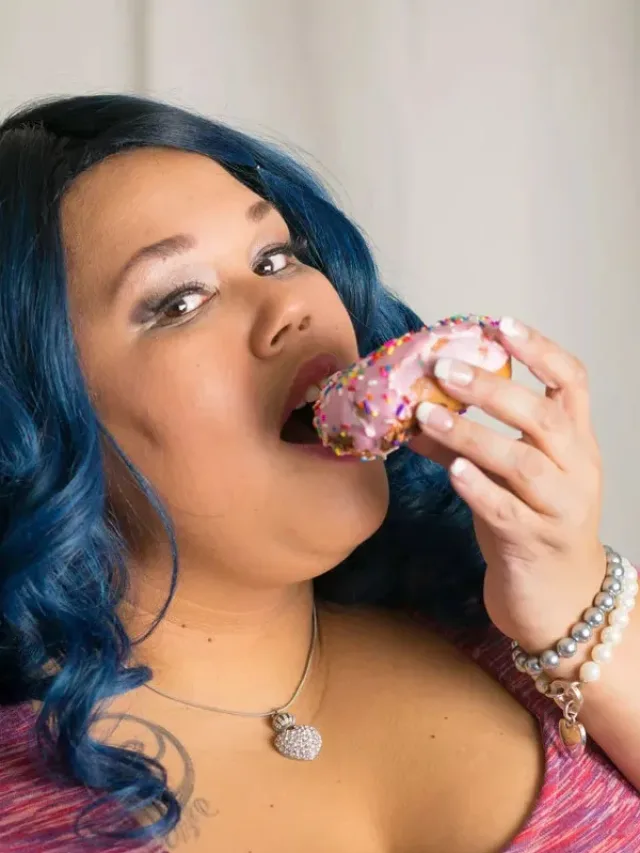 Woman in long curls eating pose with a donut in left hand