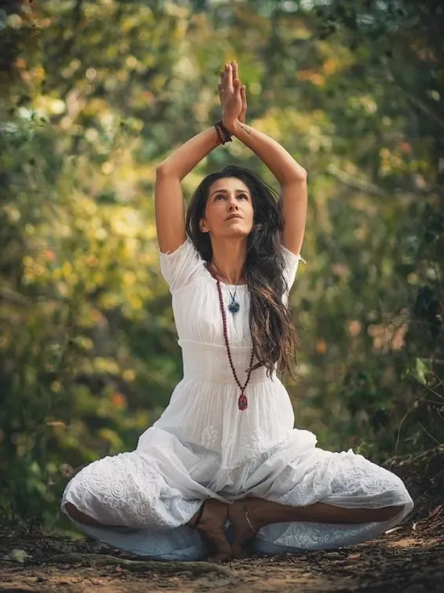 Woman in forest sitting on toe tip with hands raised and folded eye position upwards