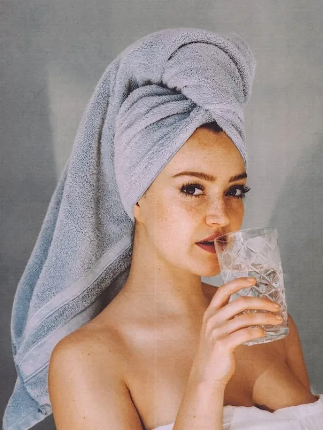 woman head covered with towel sipping a glass of water inside a wellness retreat