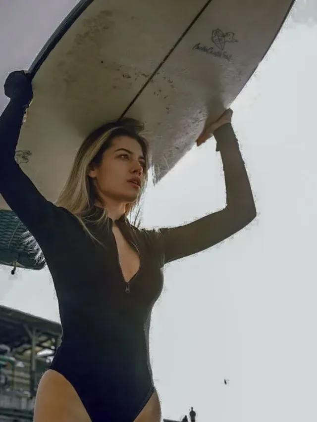 young woman in black swim suit with surf board on head