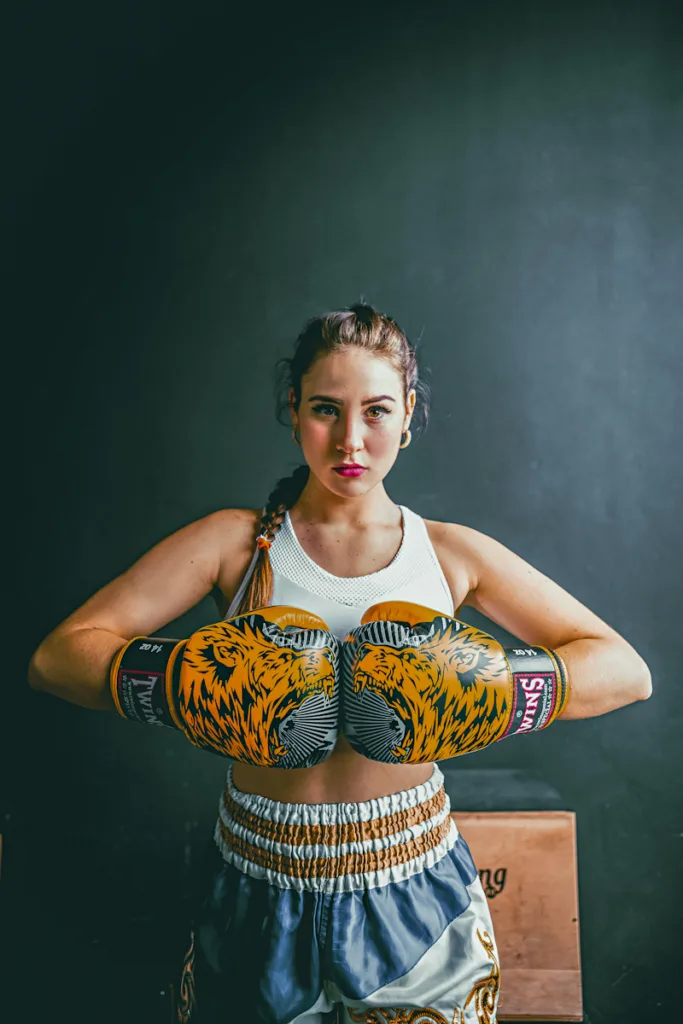 woman in white top and boxing gloves and boxing pants fisting both hands