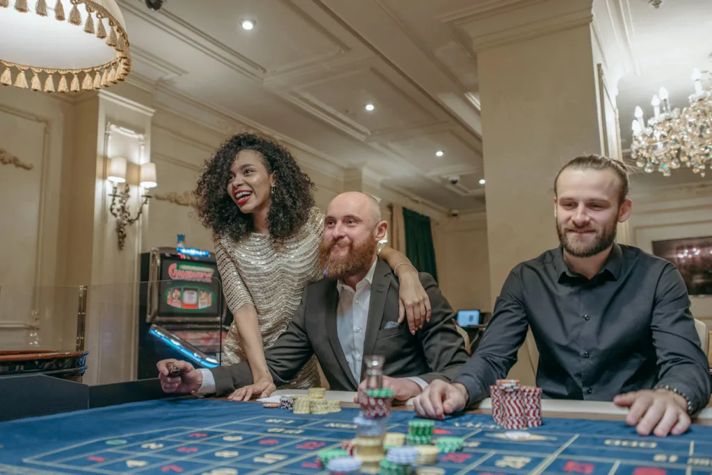 woman in golden one piece cuddling with one arm to a man in beard who is smiling on a casino table