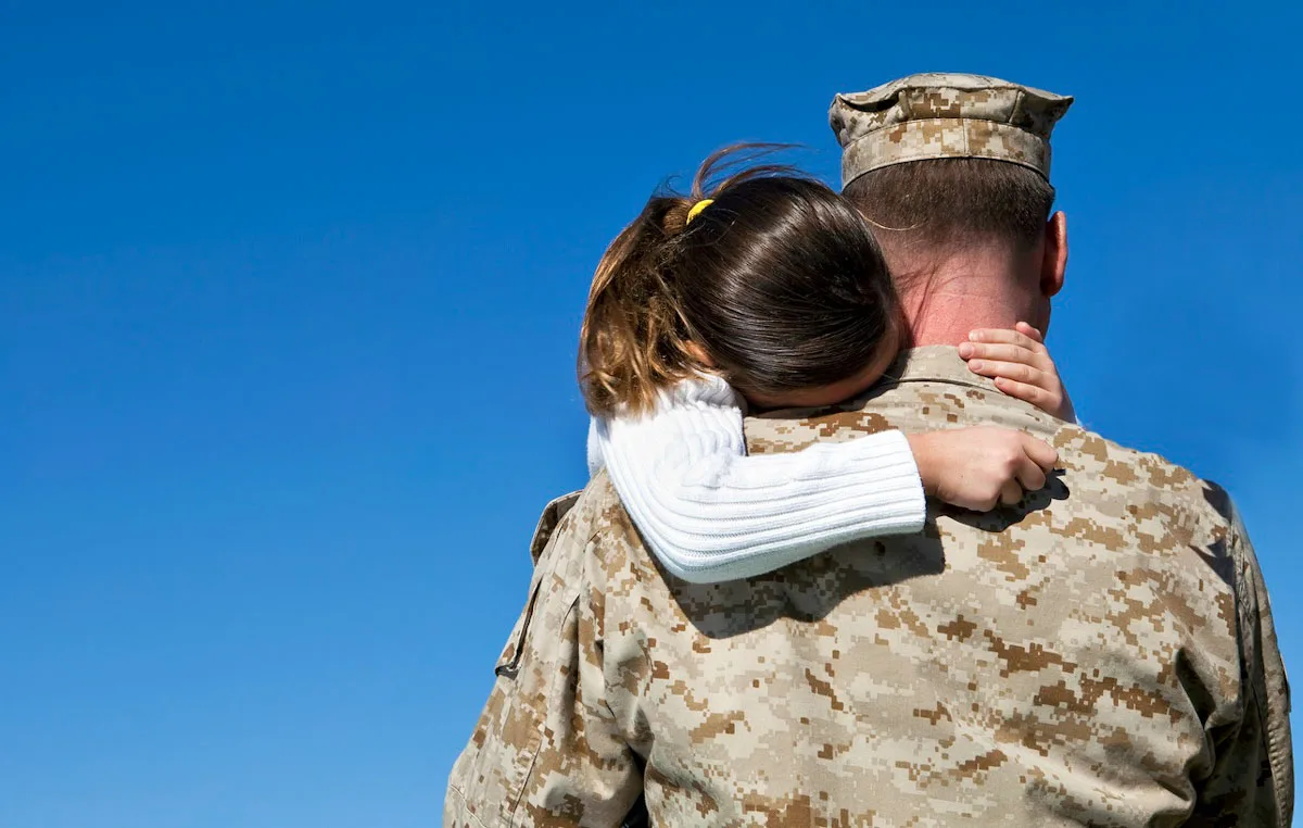 example of healing from military trauma -Military man backside angle hugged by his daughter whose face id down in his shoulder and right hand fist closed and left hand holding his neck
