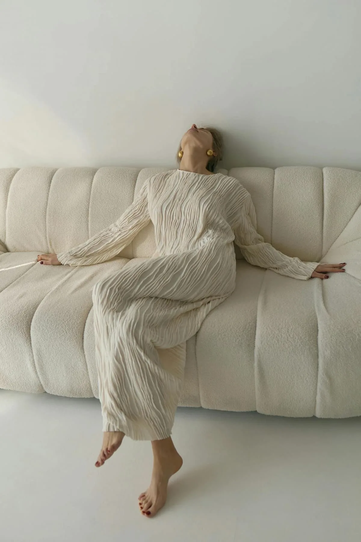 woman in off-white long dress on a sofa with head facing at the sky.