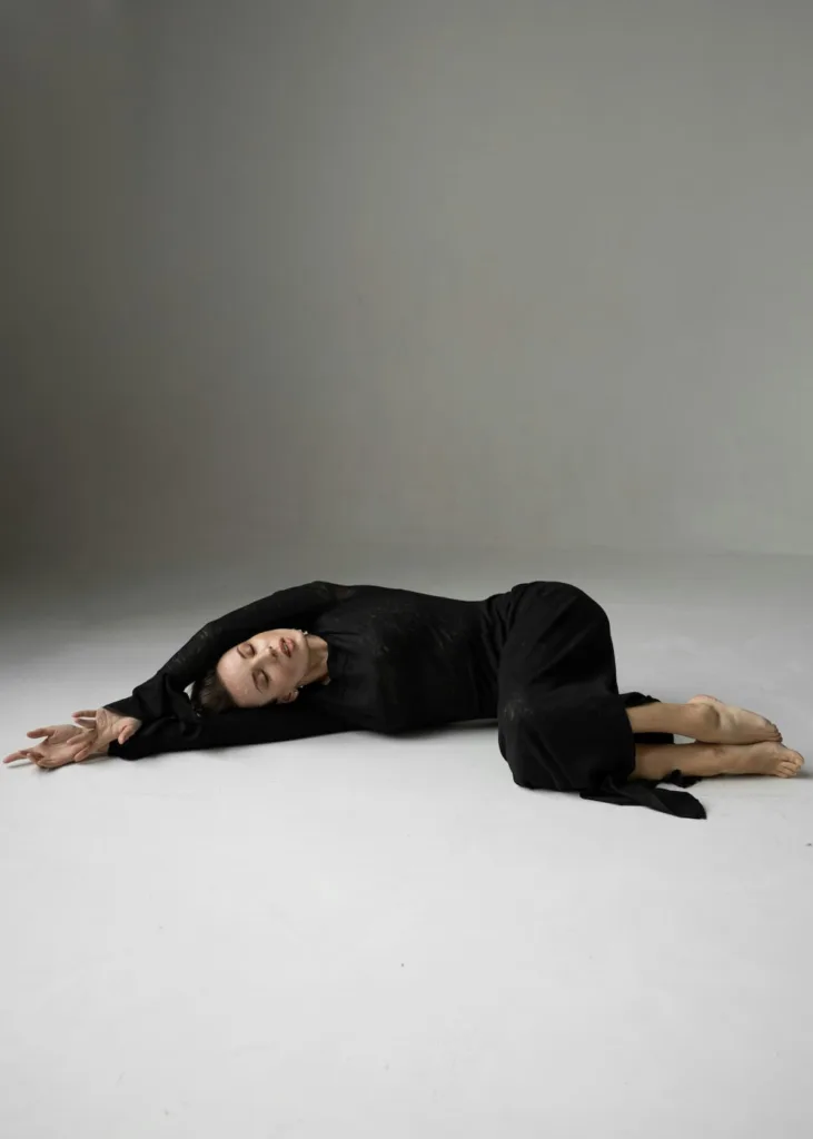 woman in long black dress with hands stretched and folded and legs half folded with closed eyes