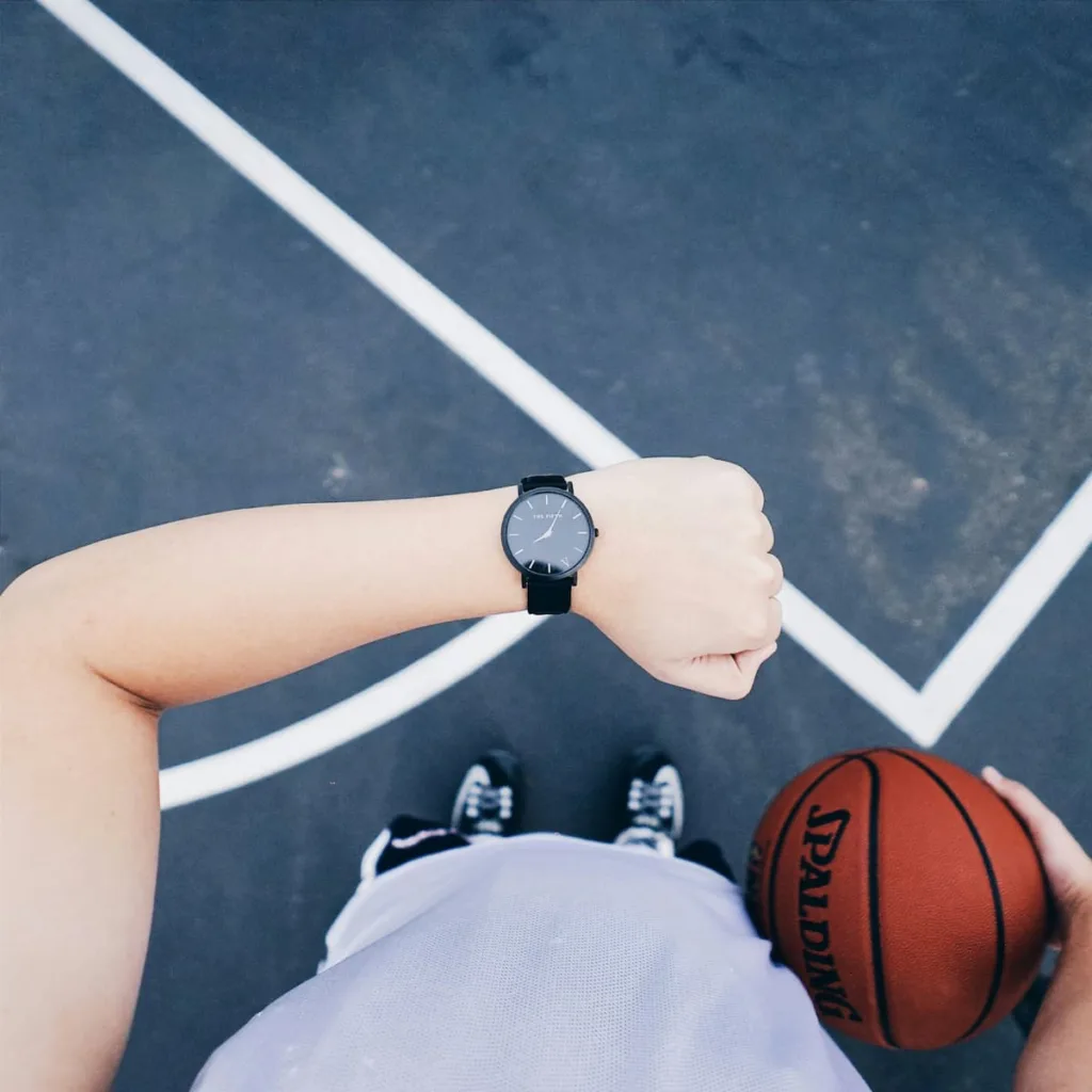 A Man watching an analog watch with basket ball in hand.