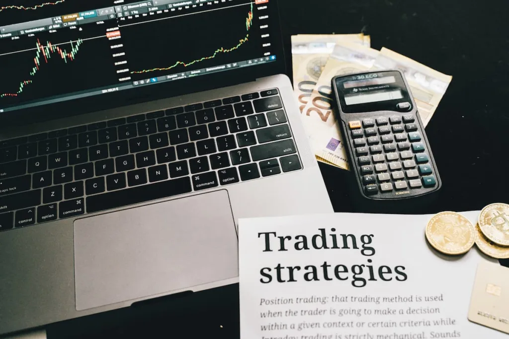 laptop next to a calculator and some money and paper with title Trading strategies.