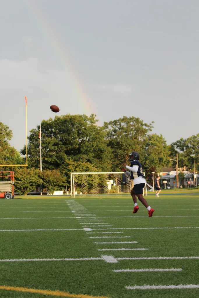 A man practicing American football inside a stadium with rainbow in landscape