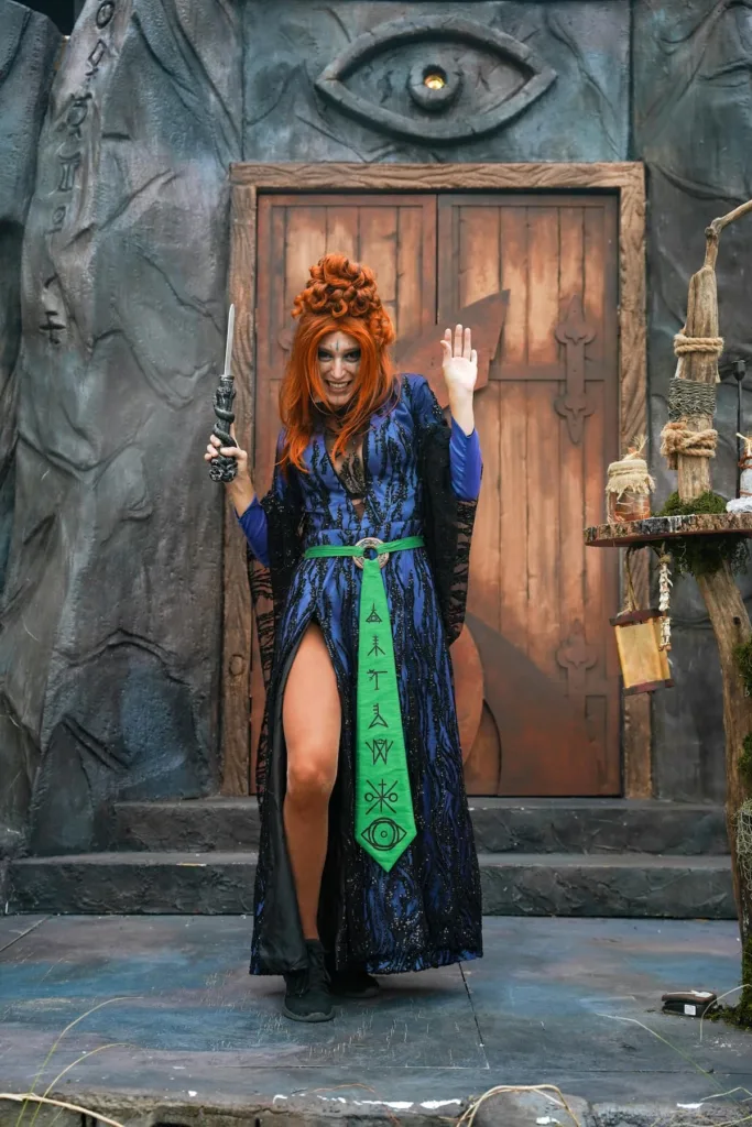 Woman in blue gown with thigh slit holding wand in one hand resembling a witch cosplay