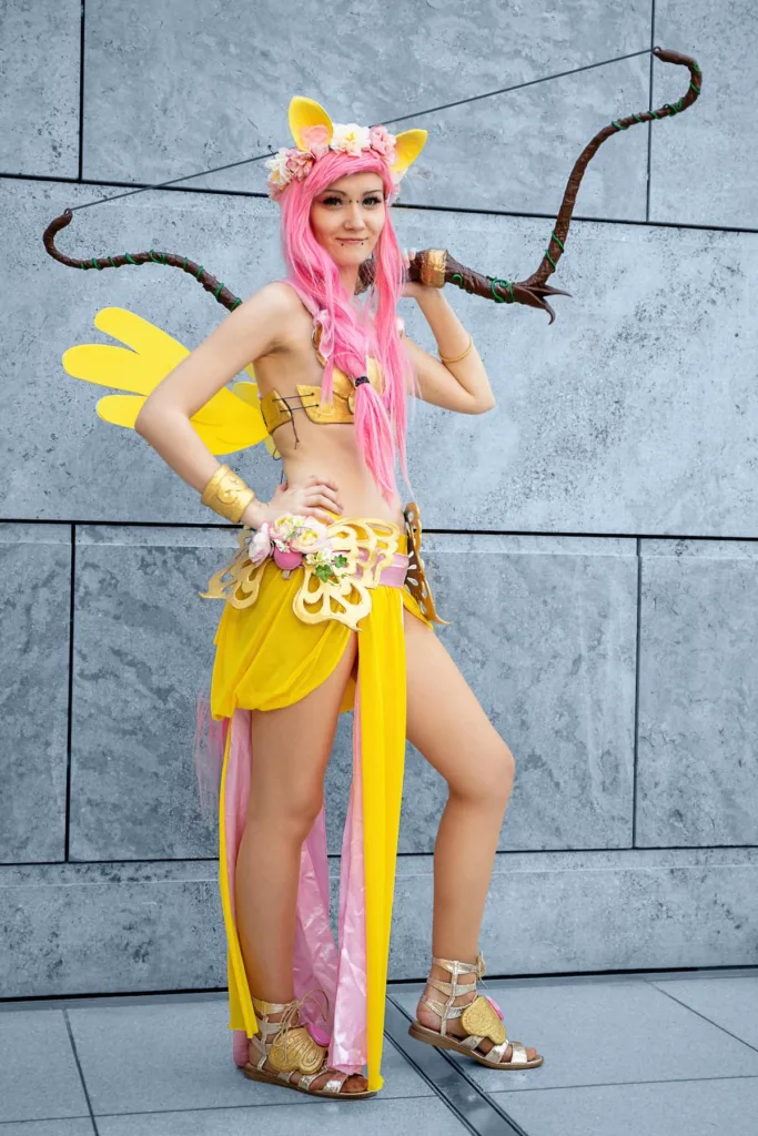 woman with bow on shoulder and other hand on waist in orange yellow cos play suit with wings Cosplay Culture at Comic