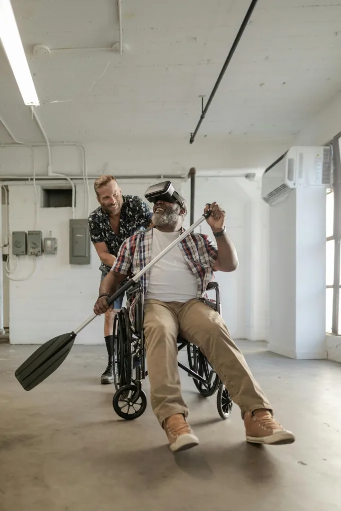 One man on wheel chair wearing VR box with paddle in hand and other man pushing the chair