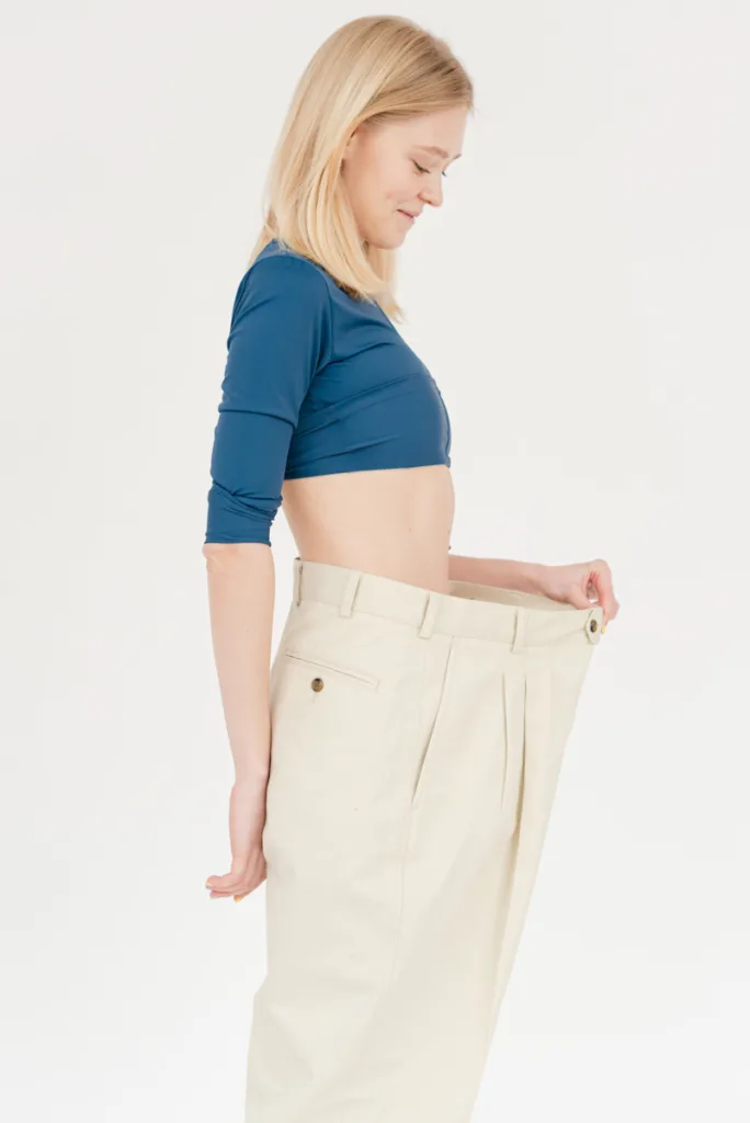 woman in aqua blue top, blonde hair and cream oversized pants holding it with left hand- Rapid Weight Loss