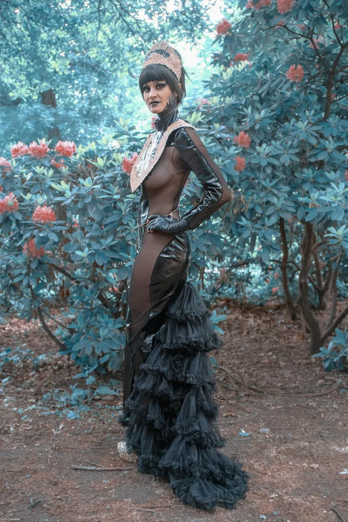 A woman in cos play suit with fishnet long gown standing near flower plants