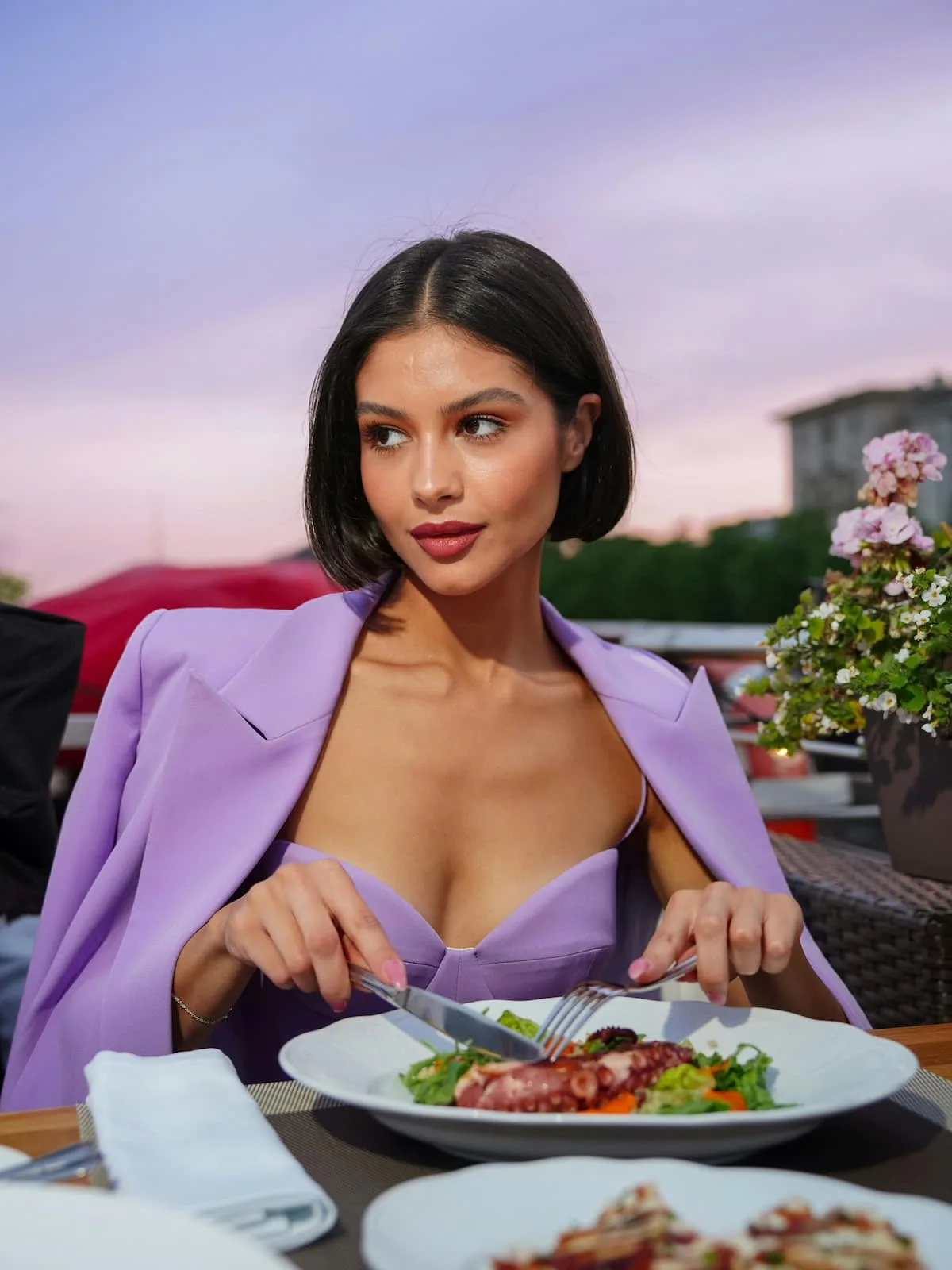 Ultra Processed Foods: Facts vs Myths woman in lavender sweat heart neck dress with lavender overcoat on shoulders using fork and knife to cut food on plate but looking sideways