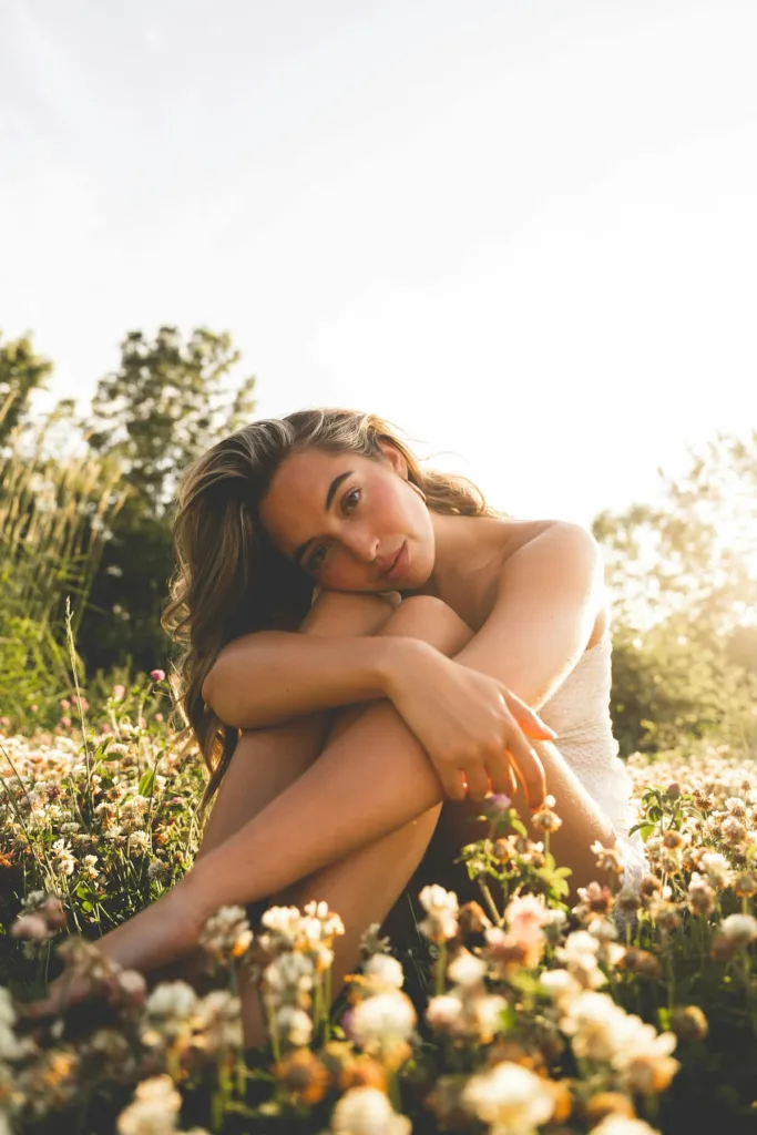 woman surrounded by flowers out in open with blonde hair sitting with raised legs and hugging legs with hands and thinking - Understanding Women with ADHD